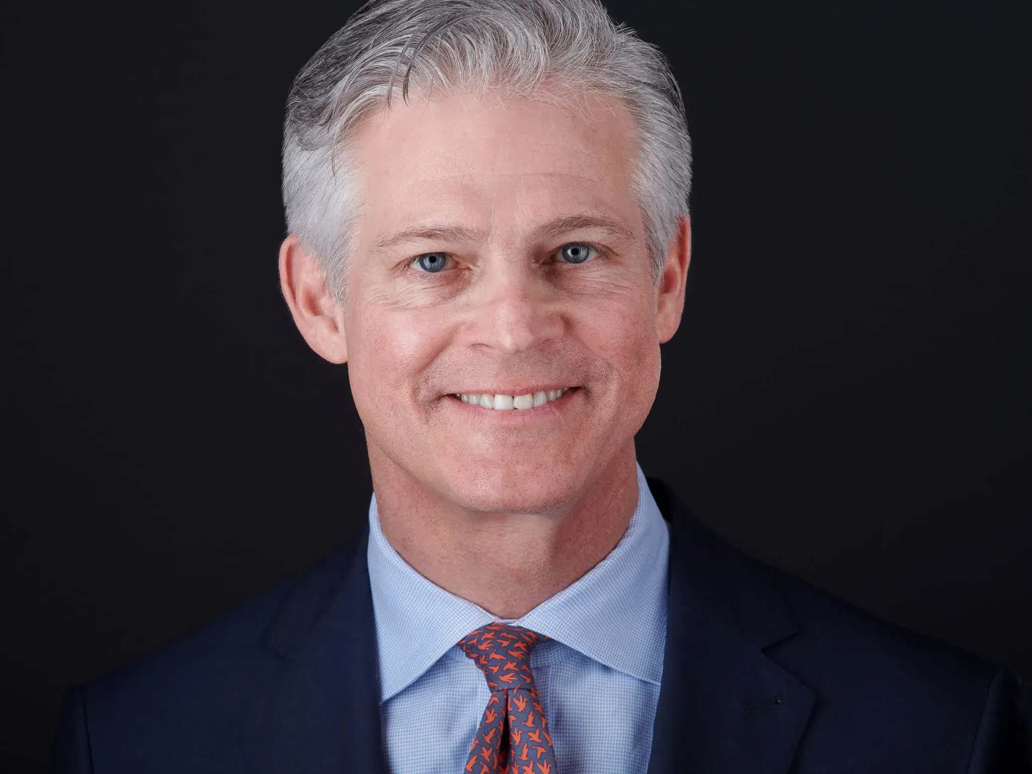 Professional headshot cropped just above the hairline — eyes in the upper third of the frame, face fills the image, stronger and more commanding presence