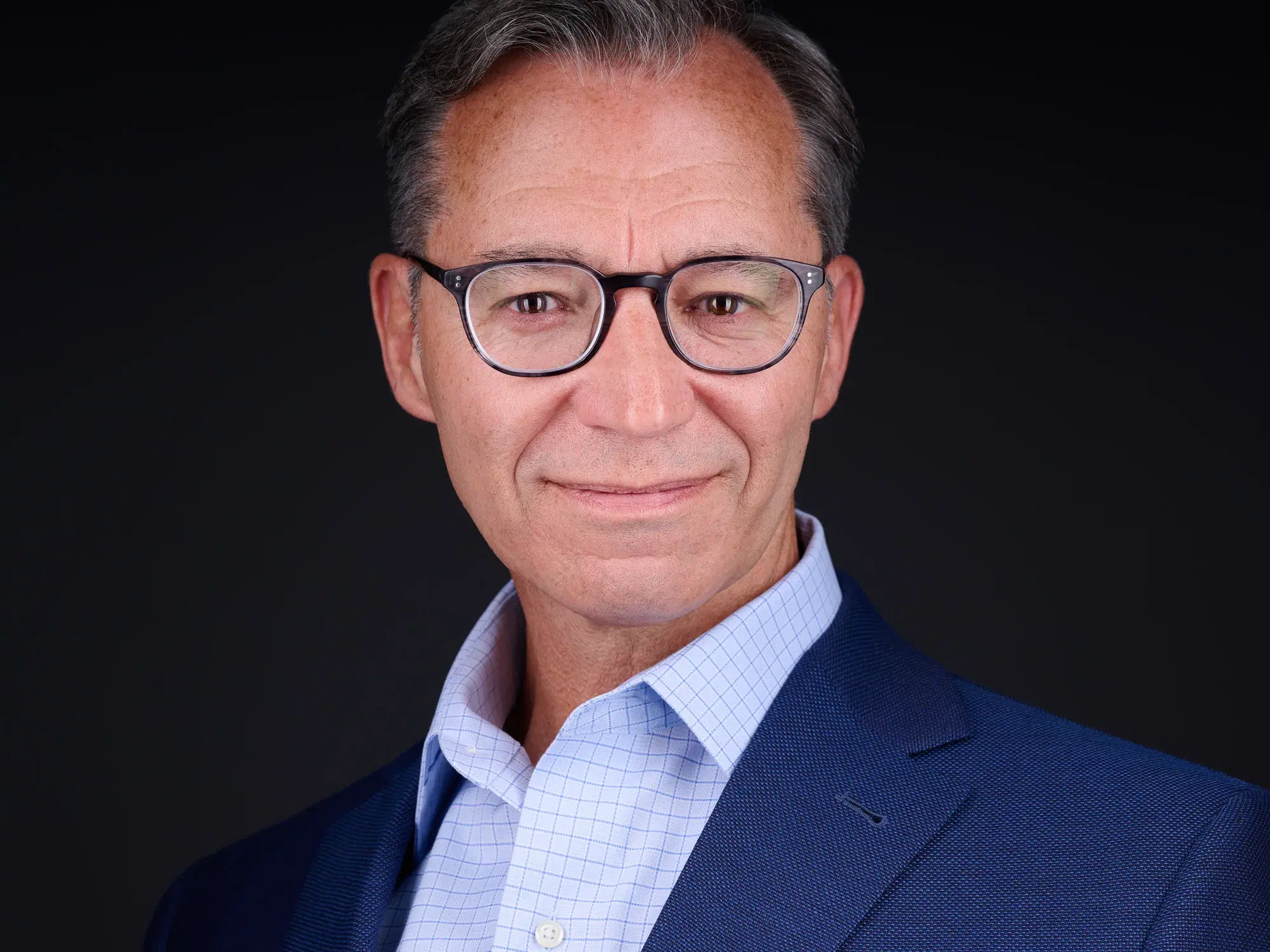 Professional headshot of man in light blue checkered shirt and navy blazer with friendly expression against gray backdrop — Boston executive headshot photographer Damon Bates Photography