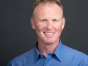 Headshot of a smiling man in a blue shirt against a gray studio backdrop, by Damon Bates Photography