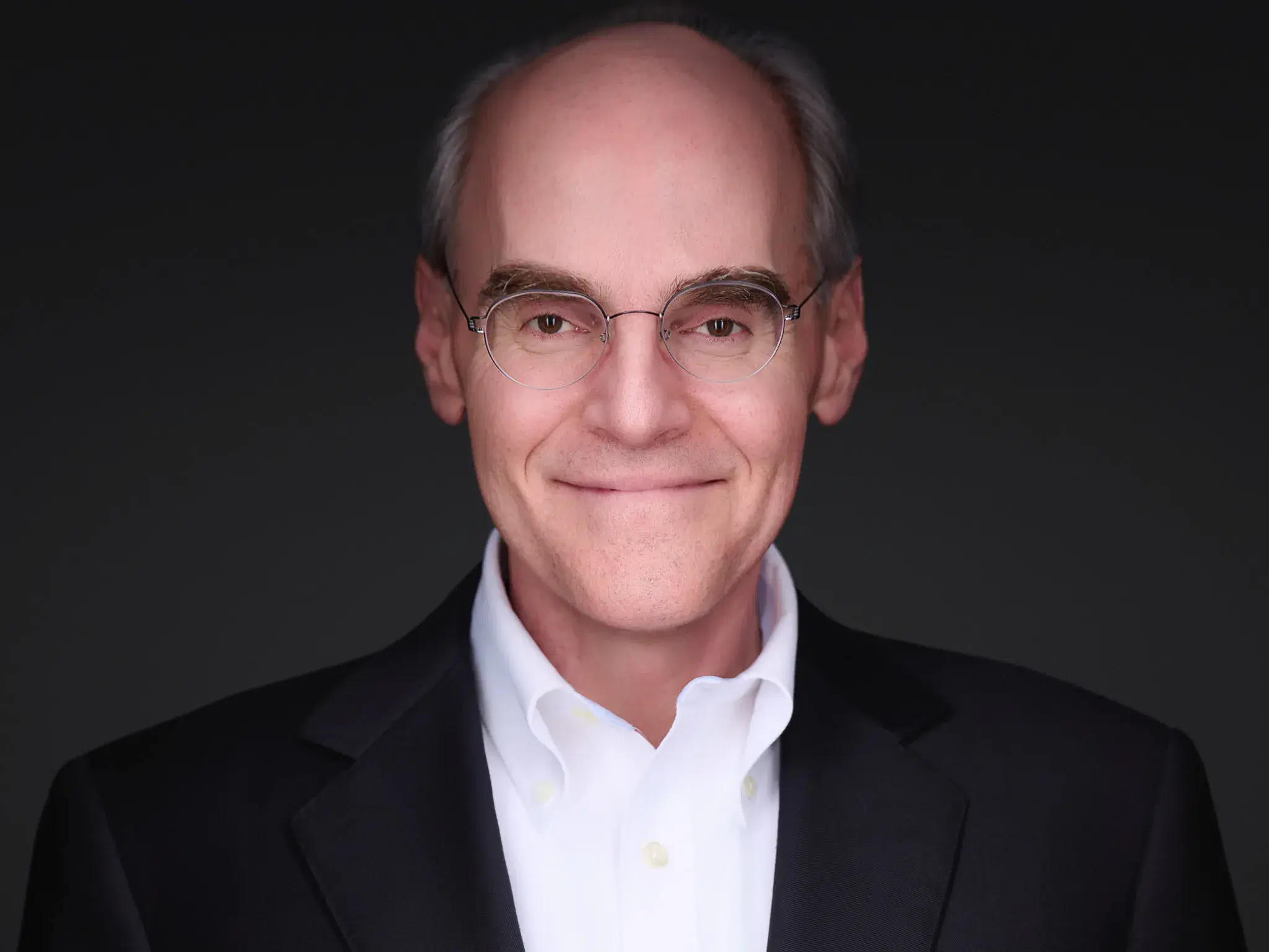 Executive headshot of a man in a dark suit with a white shirt worn under the jacket